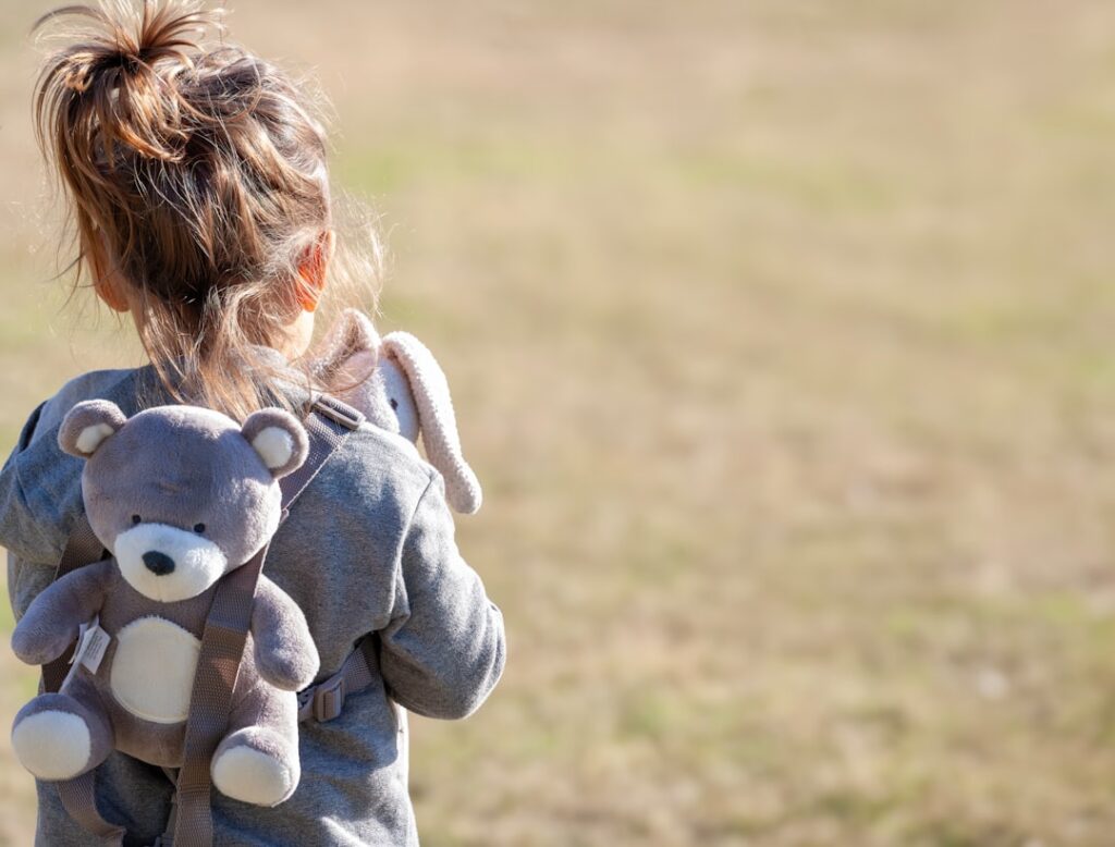 a little girl holding a teddy bear in a field
