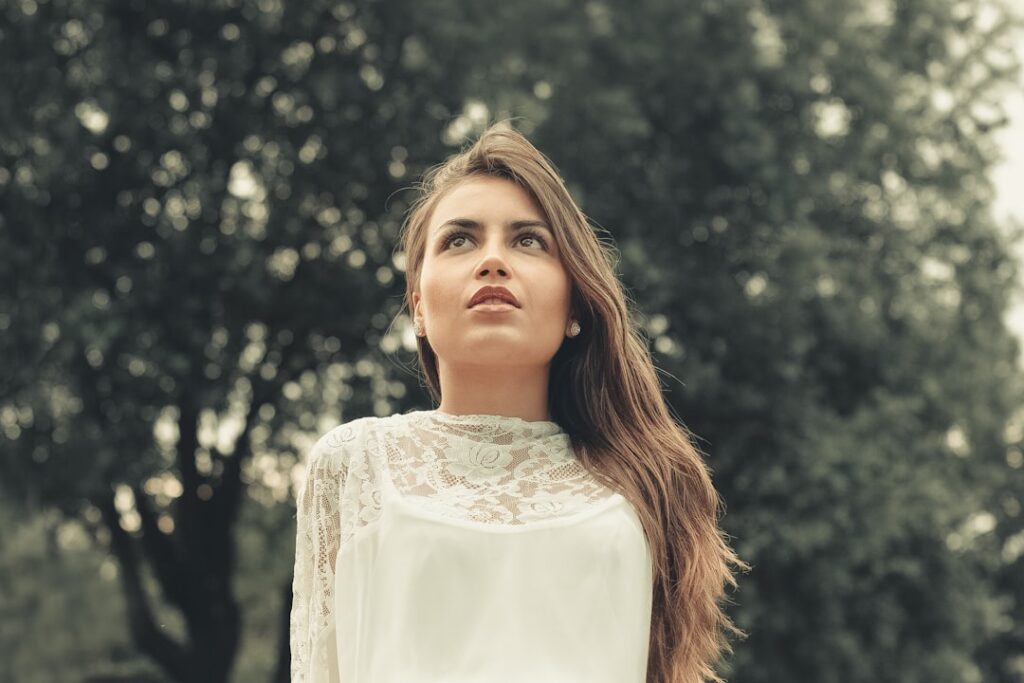 woman in white floral dress standing near green trees during daytime