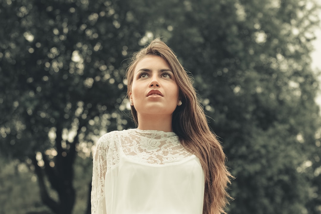 woman in white floral dress standing near green trees during daytime